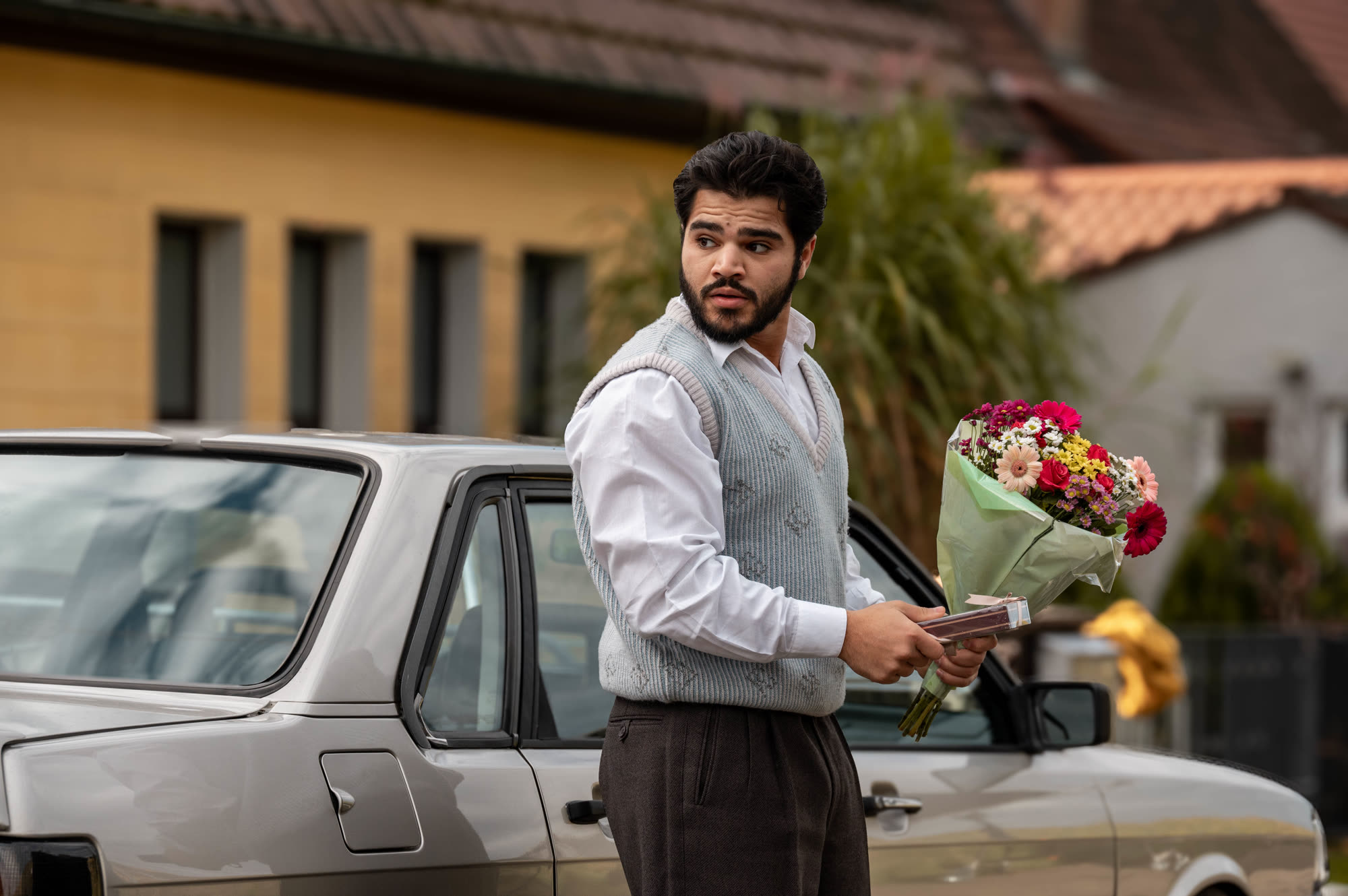 Szene aus Für Sibel: Ein junger Mann mit Blumenstrauß vor einem Auto