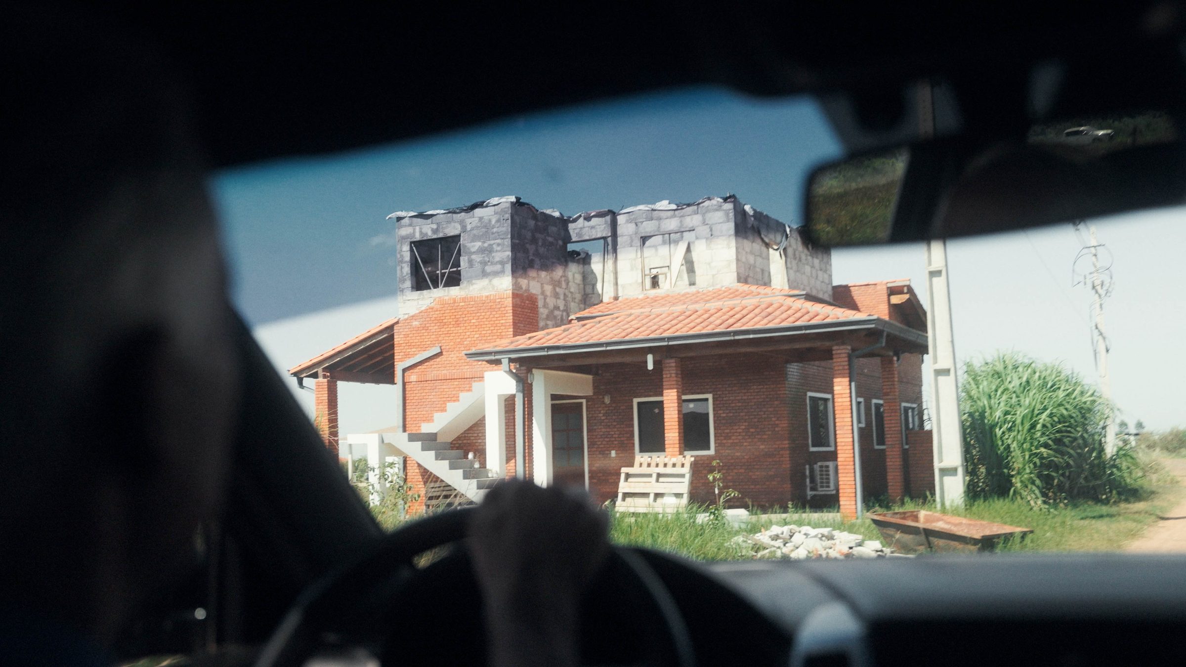 Szene aus Im Umkreis des Paradieses: Blick aus einem Auto auf ein Backsteinhaus im Rohbau