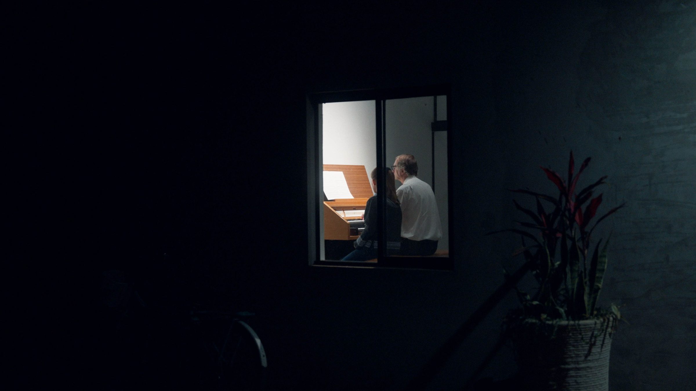 Szene aus Im Umkreis des Paradieses: Zwei Personen in einem erleuchteten Fenster eines dunklen Hauses